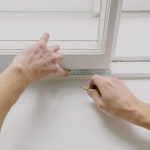 A photograph of a persons hands, with a tape measure against a window